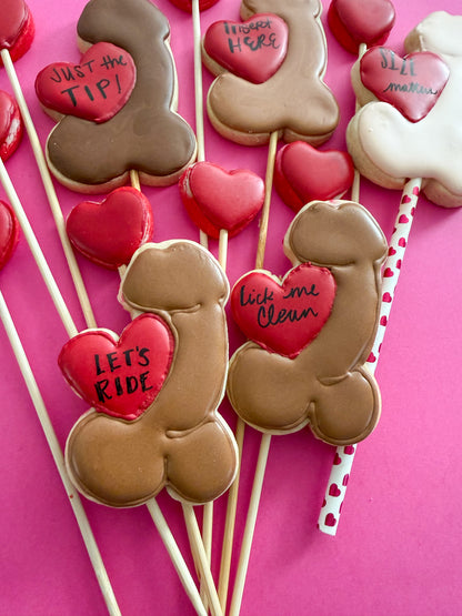 Decorative cookies on sticks with heart-shaped with penis cookies against a pink background