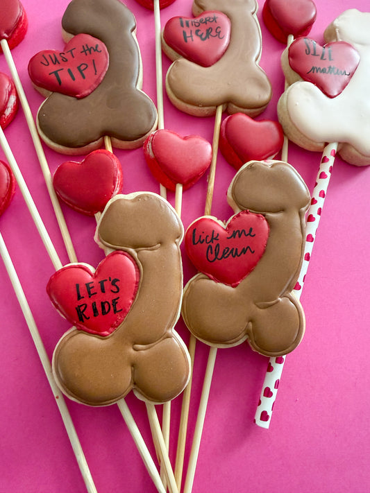 Decorative cookies on sticks with heart-shaped with penis cookies against a pink background