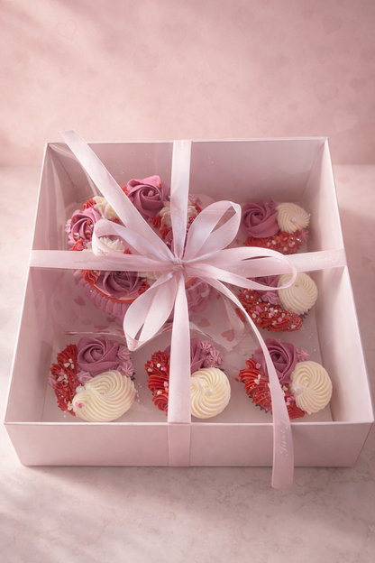 Decorative box with pink, red, and white cupcake-shaped candies on a light pink background