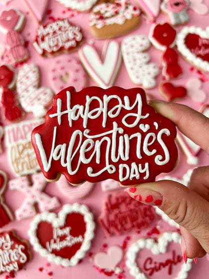 Hand holding a 'Happy Valentine's Day' cookie with more cookies in the background